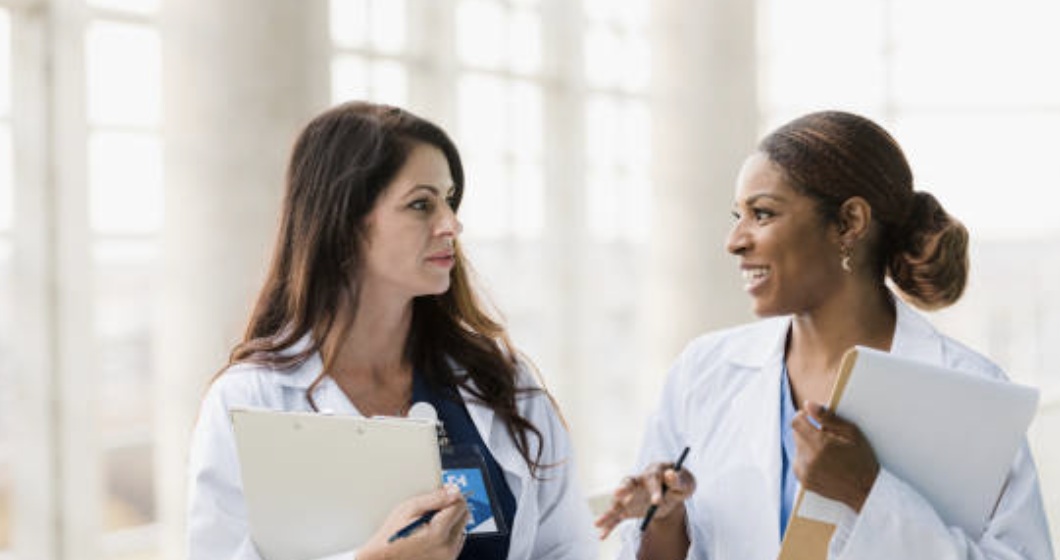 Stock placeholder showing two clinicians talking in a bright hallway; not Kim and Leah